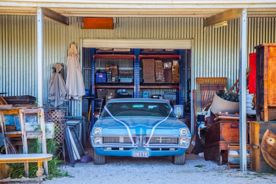 A blue classic car surrounded by antique furniture at the Zin House Garage